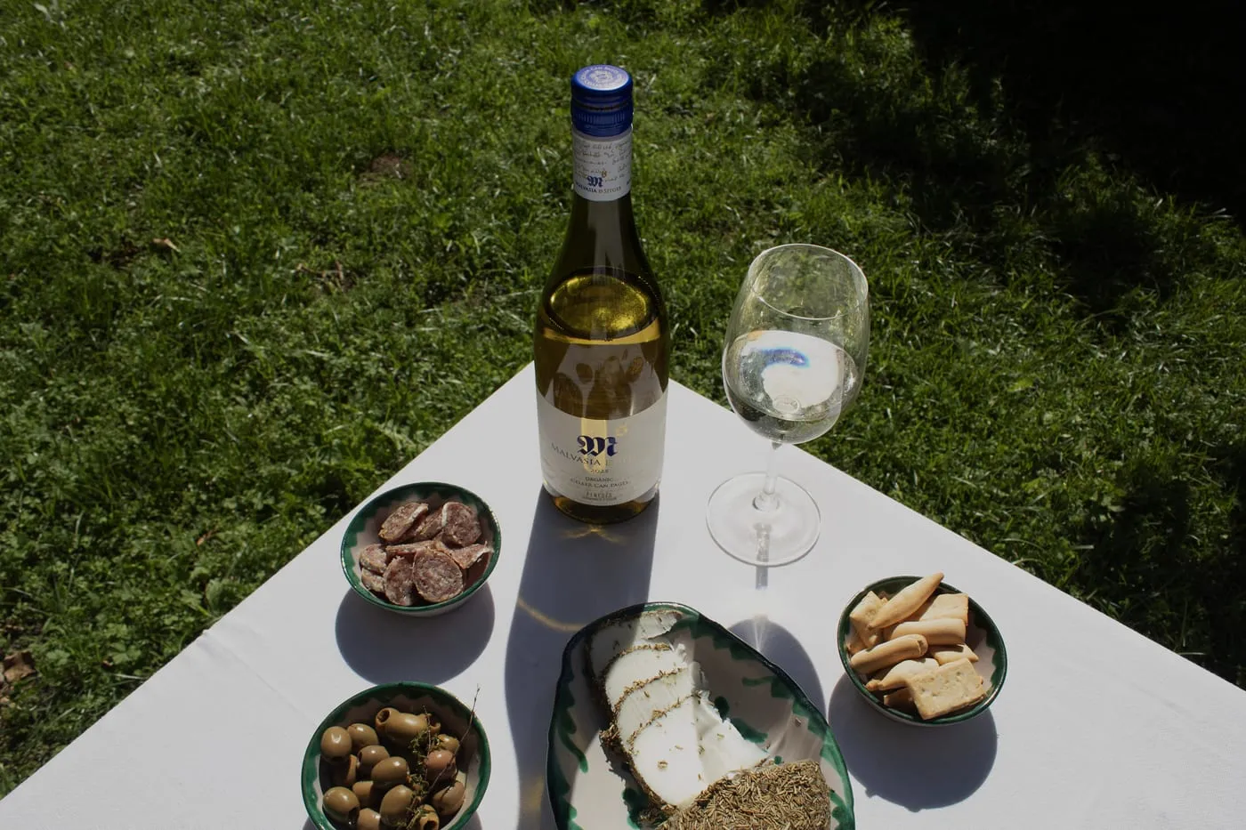 Taula amb una ampolla de Malvasia de Sitges i maridatge d'embotits, formatge i olives